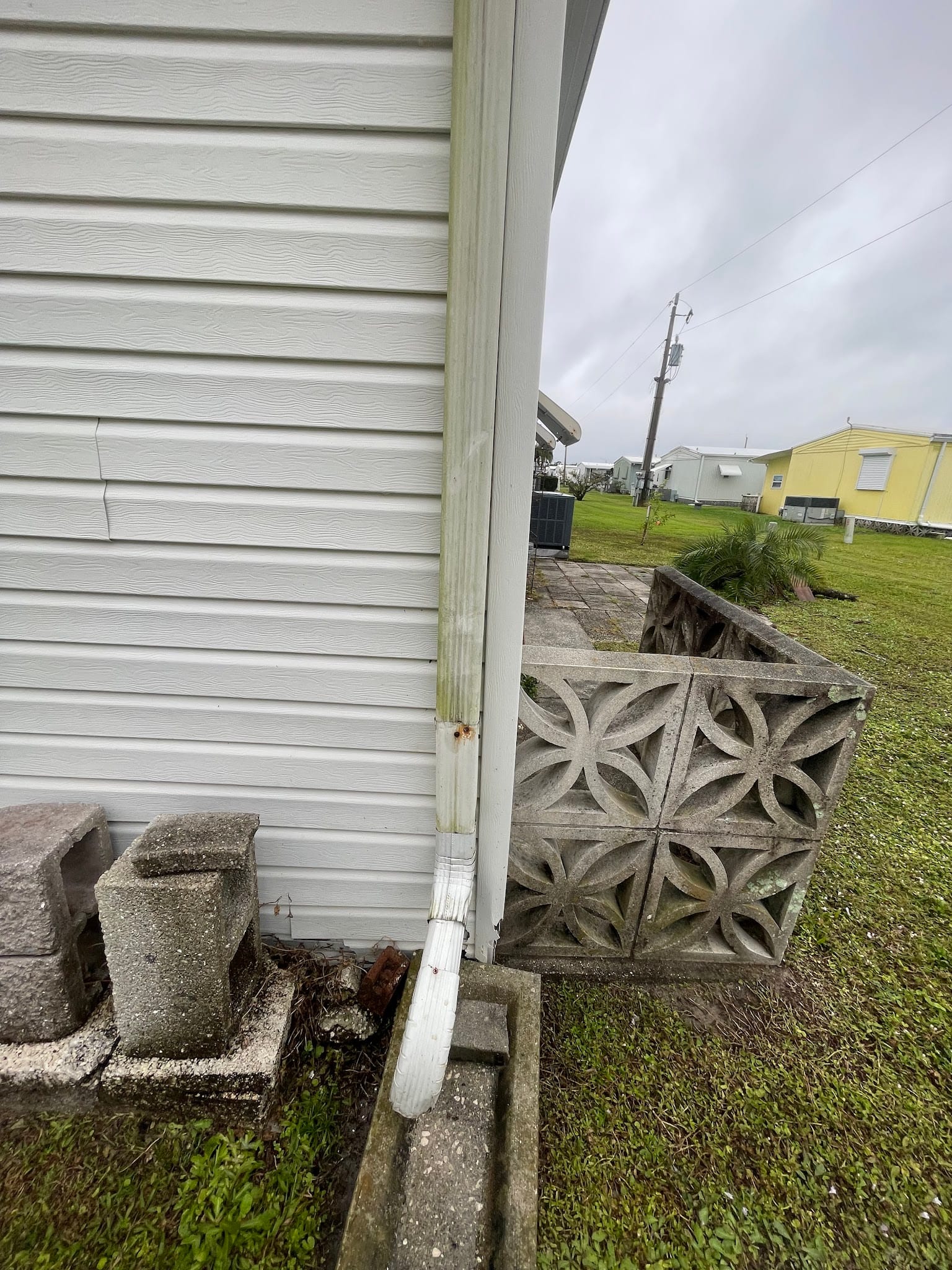 Dirty downspout with debris buildup on white vinyl siding home