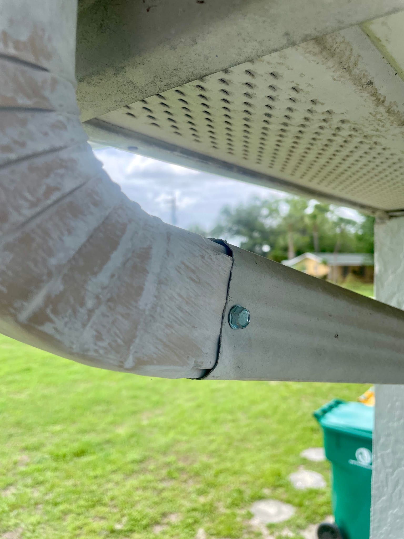 Close-up of a metal gutter downspout elbow connection secured with a bolt