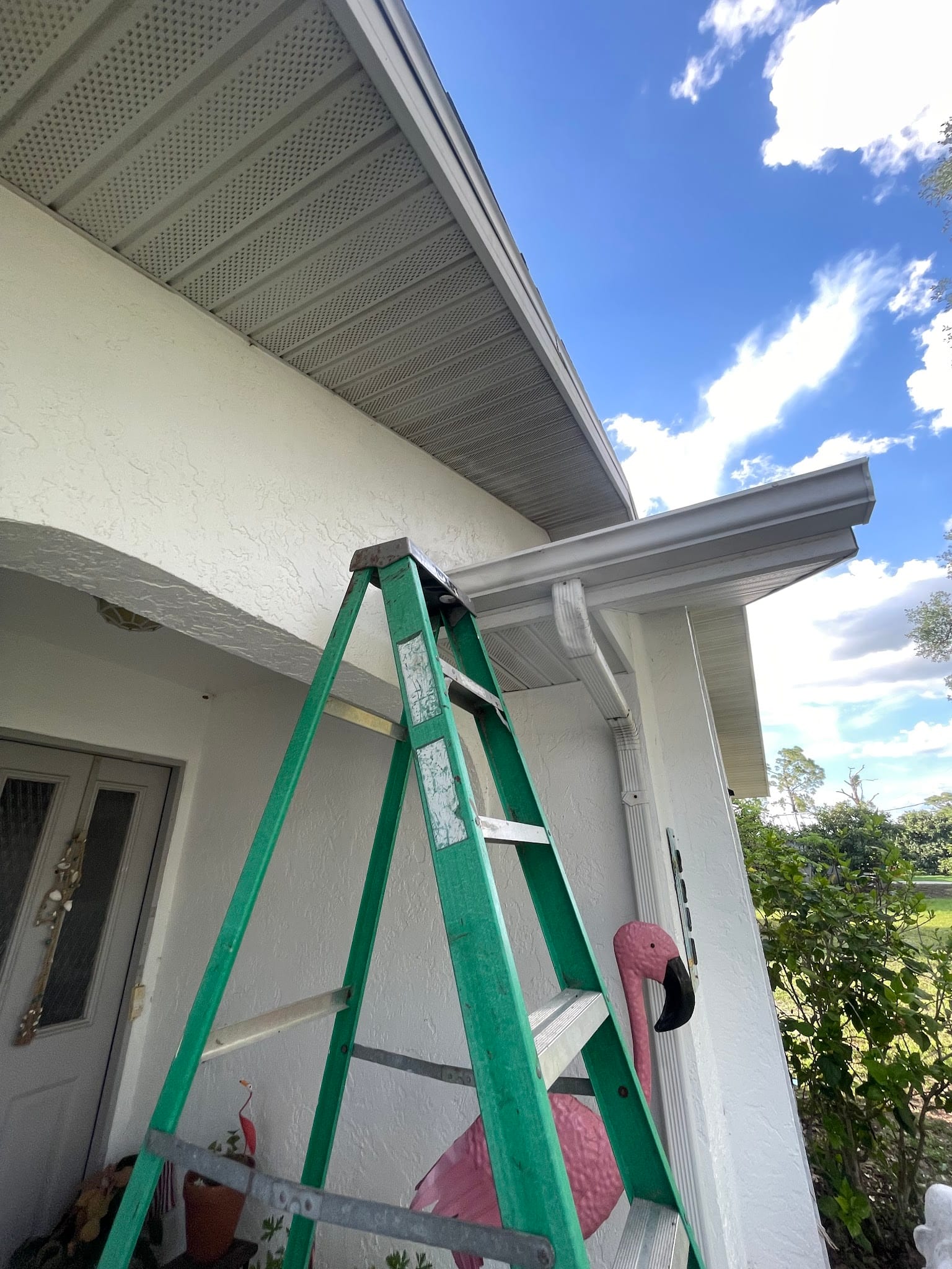 Green ladder positioned against white stucco home near gutters and downspout