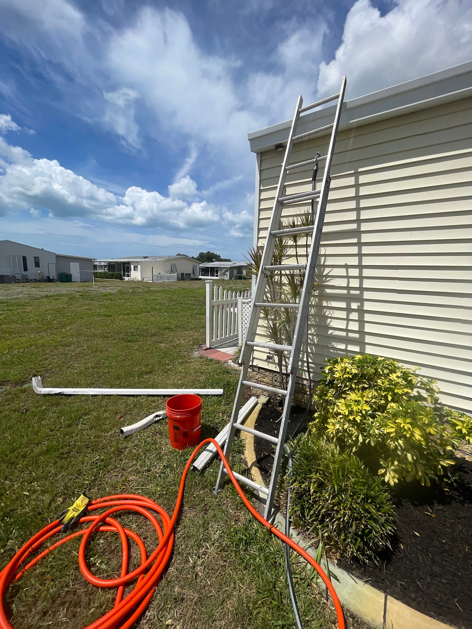 Aluminum ladder leaning against home siding with gutter cleaning tools nearby