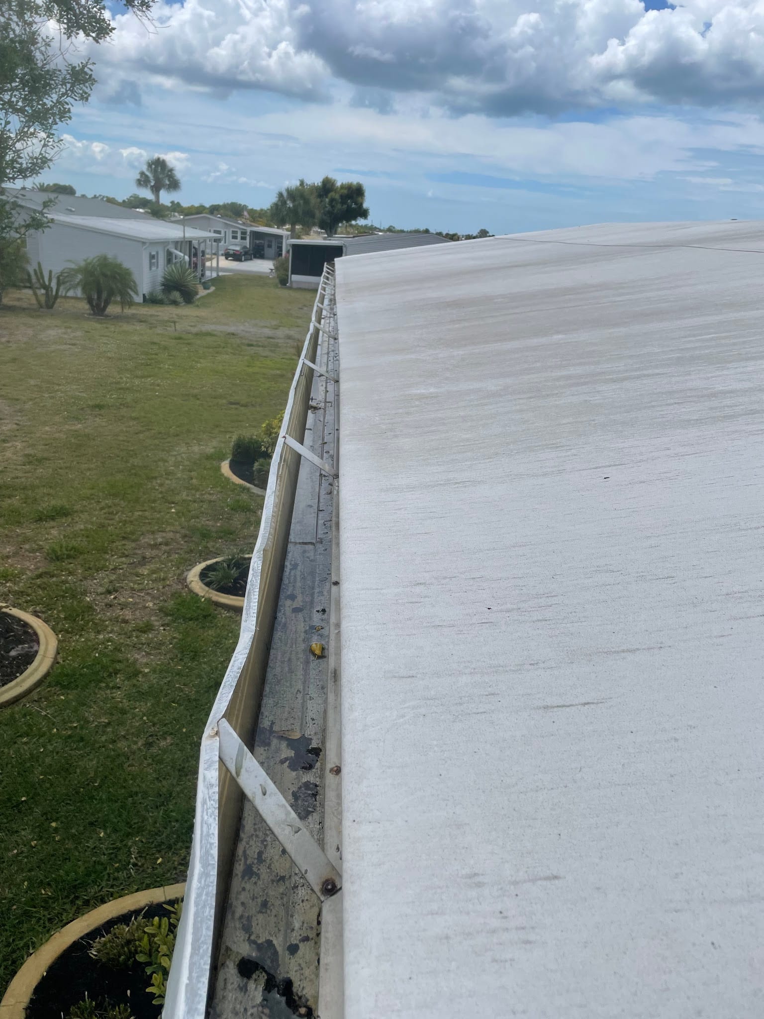 Dirty gutter with debris along white mobile home roof edge in Port Charlotte