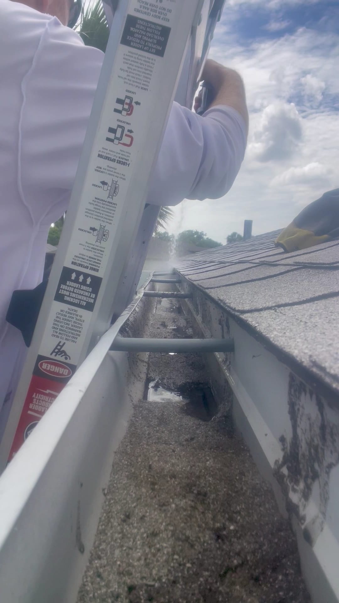 Technician on ladder clearing debris from clogged residential gutter