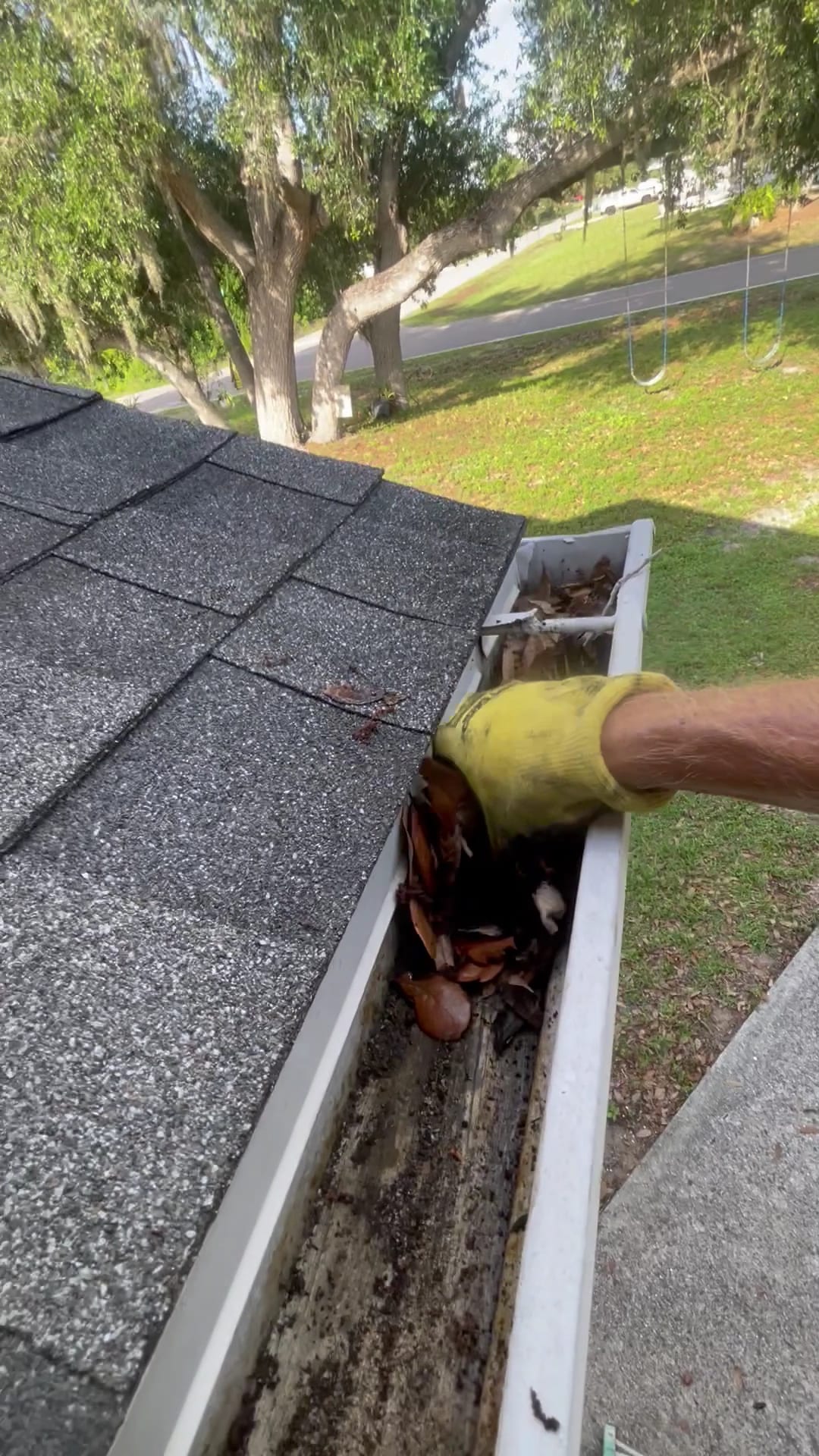 Gloved hand removing leaves and debris from clogged white rain gutter